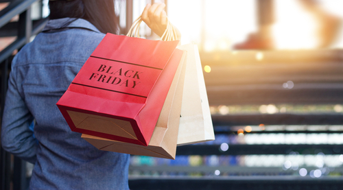 Imagem mostra mulher de costas segurando sacolas de compras e em uma delas está escrito "Black Friday"