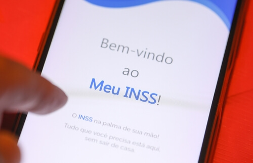 Imagem mostra mão segurando um celular que mostra a tela de início do aplicativo Meu INSS