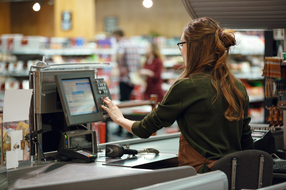 Imagem mostra mulher mexendo em tela de um caixa de supermercado