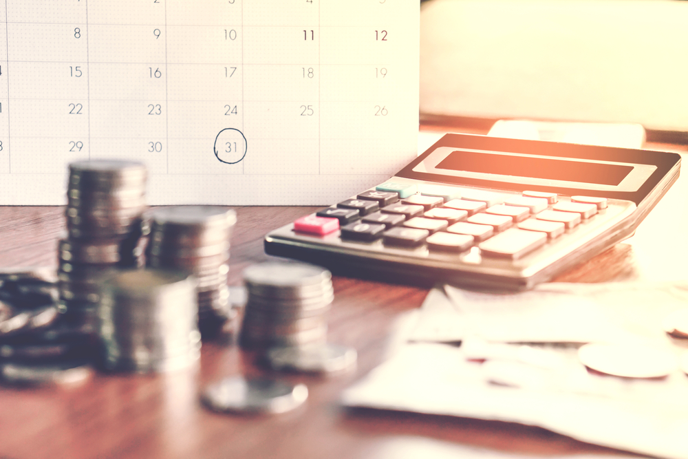 Imagem mostra uma calculadora, um calendário de mesa e moedas
