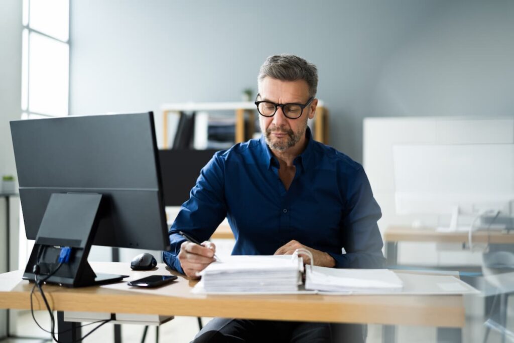 Um homem em sua mesa de escritório, com um computador e papéis