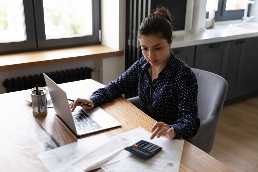 Uma mulher em seu escritório, mexendo em seu computador e na calculadora ao mesmo tempo