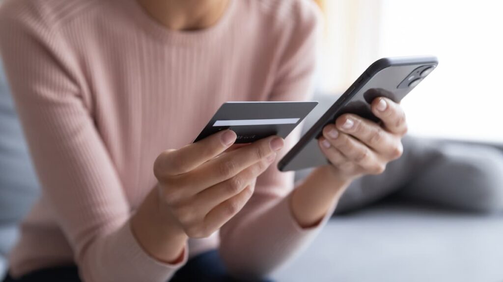 Uma mulher acessa seu banco digital através do smartphone. Ela também segura um cartão de crédito.