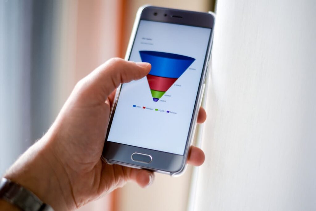 Uma pessoa segurando um celular onde, na sua tela aparece uma pirâmide invertida com os tópicos do funil de vendas