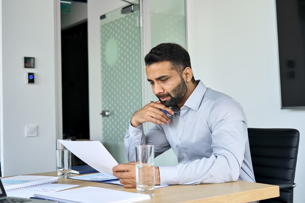 Um homem em um escritório, lendo um papel que está em sua mesa.