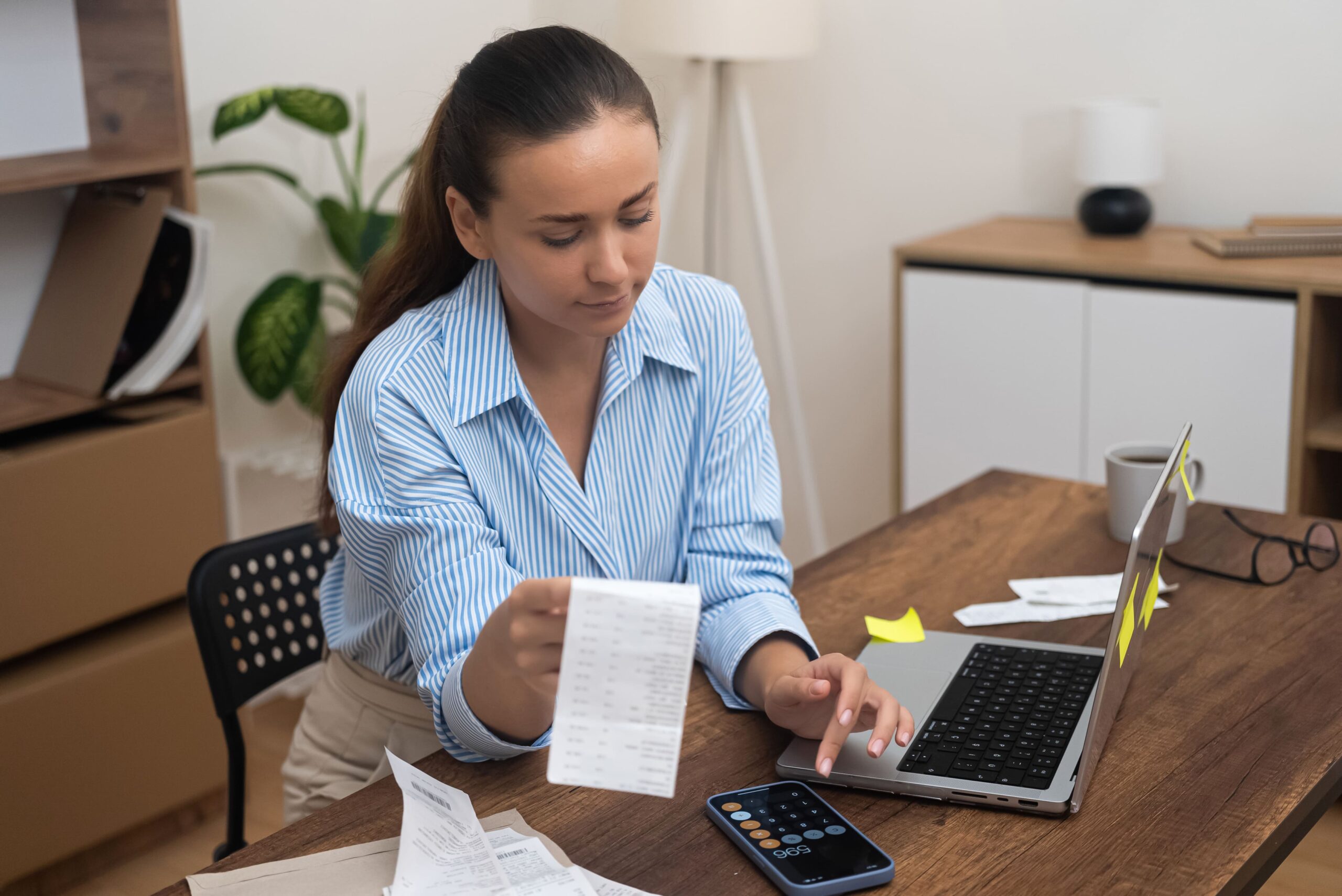 Mulher analisando contas, impostos e alíquotas em calculadora.